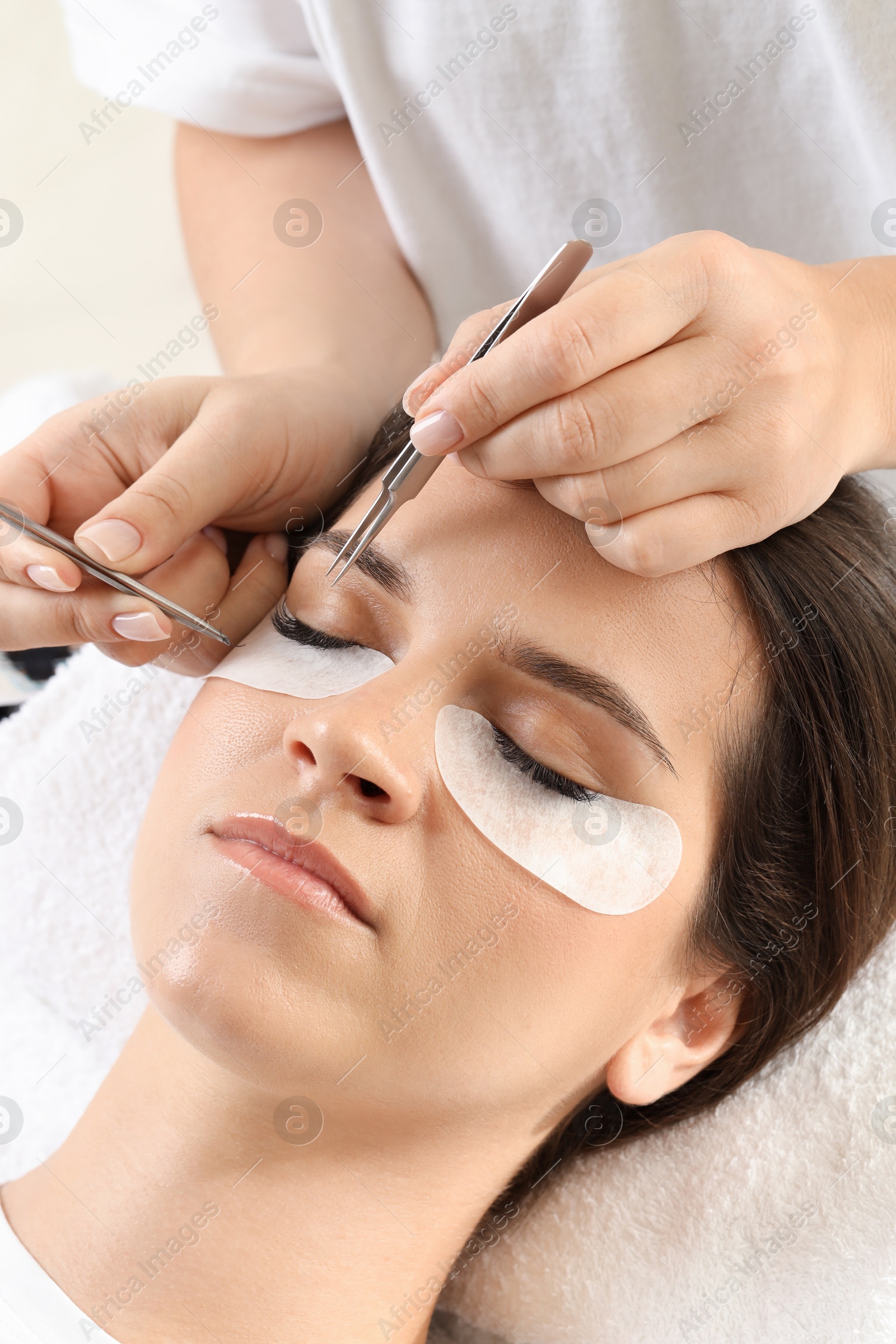 Photo of Woman undergoing lash extensions procedure in beauty salon, closeup