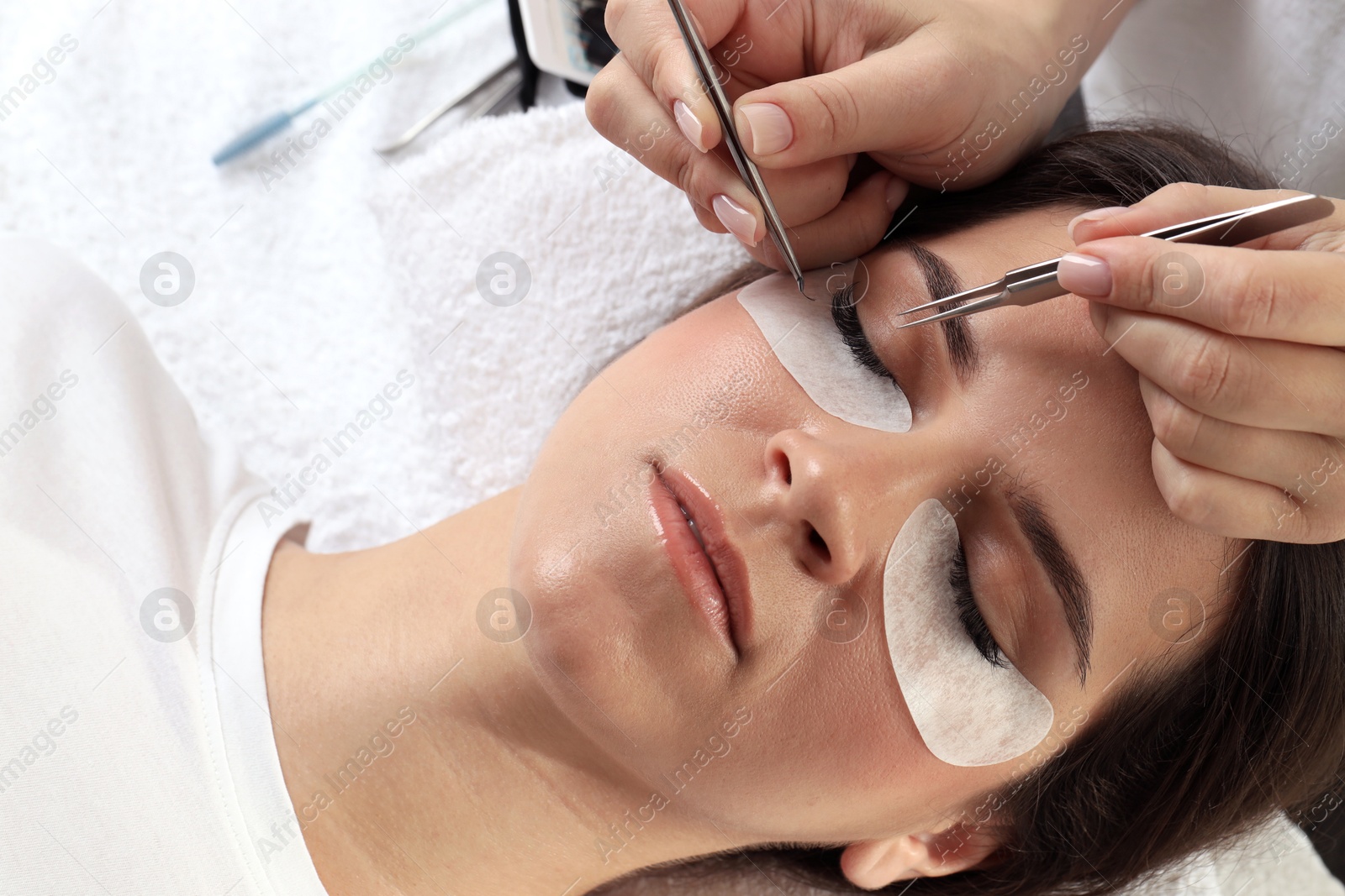 Photo of Woman undergoing lash extensions procedure in beauty salon, closeup