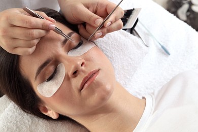 Photo of Woman undergoing lash extensions procedure in beauty salon, closeup