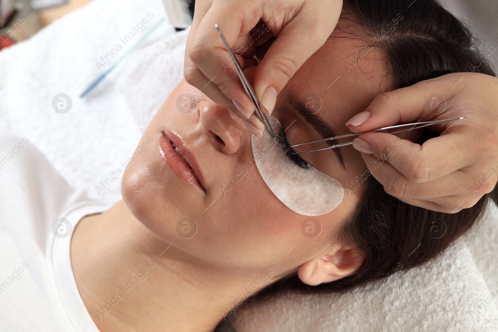 Photo of Woman undergoing lash extensions procedure in beauty salon, closeup