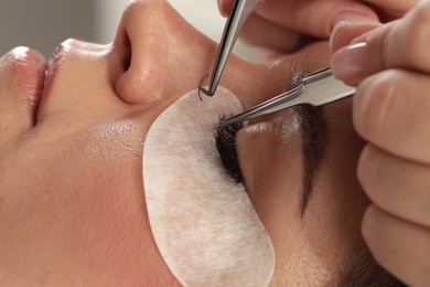 Photo of Woman undergoing lash extensions procedure in beauty salon, closeup