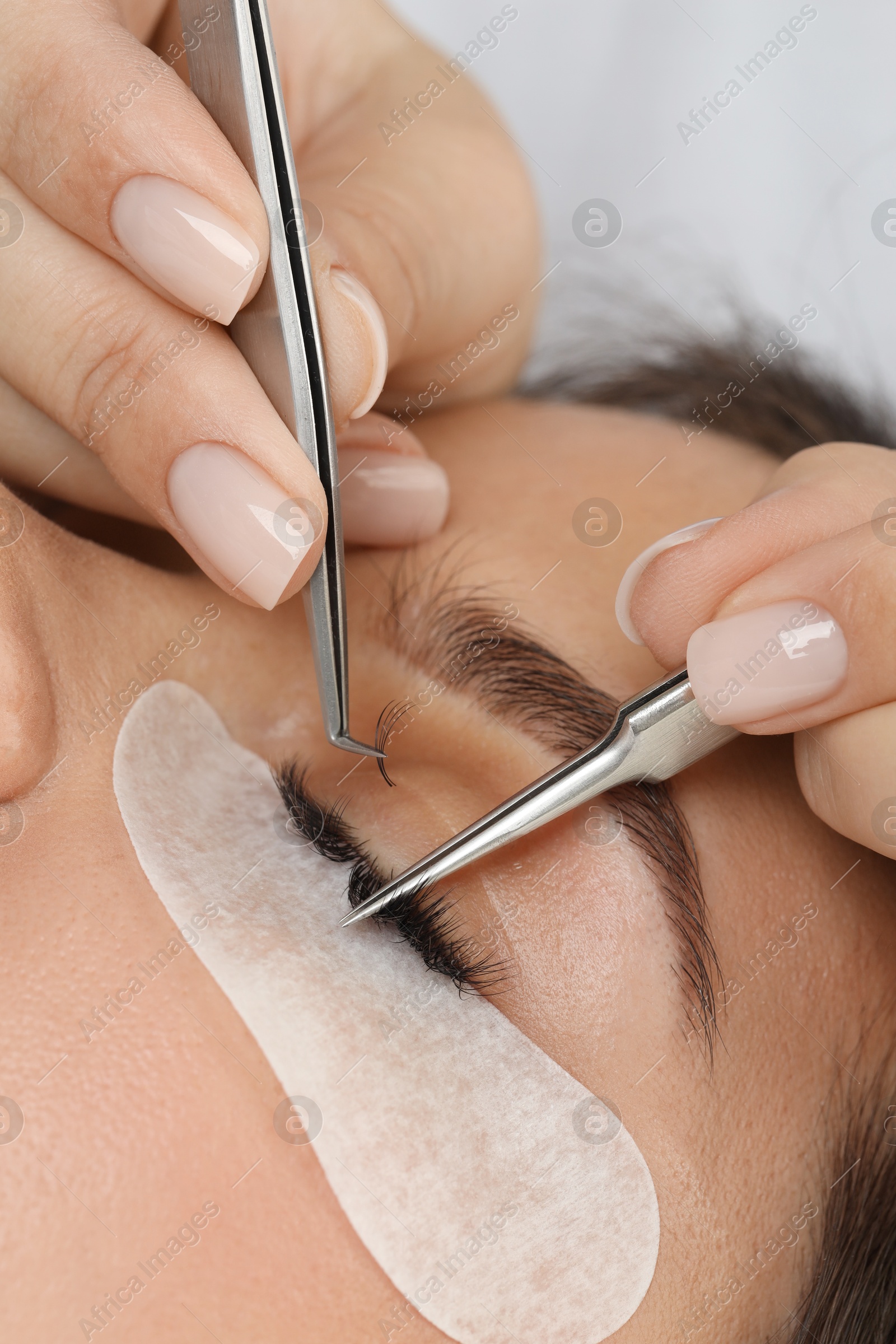 Photo of Woman undergoing lash extensions procedure in beauty salon, closeup