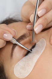 Woman undergoing lash extensions procedure in beauty salon, closeup