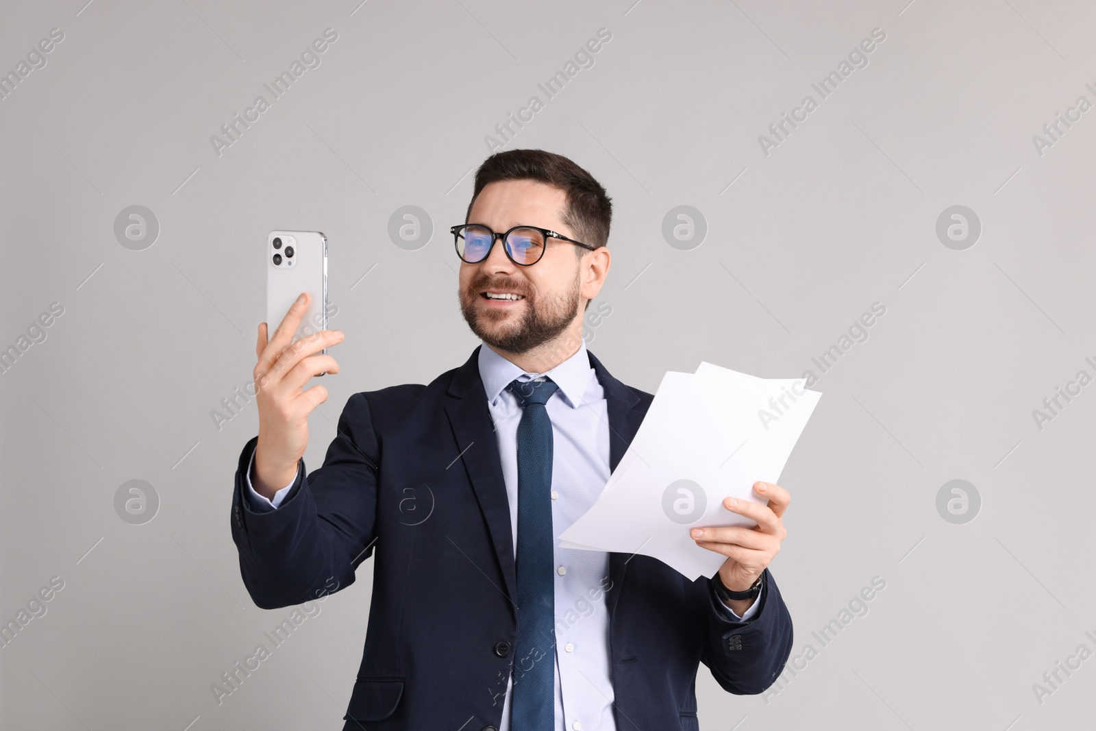 Photo of Banker with documents having video chat via smartphone on grey background