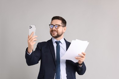 Banker with documents having video chat via smartphone on grey background