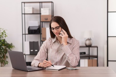 Photo of Banker talking on smartphone while working at wooden table in office