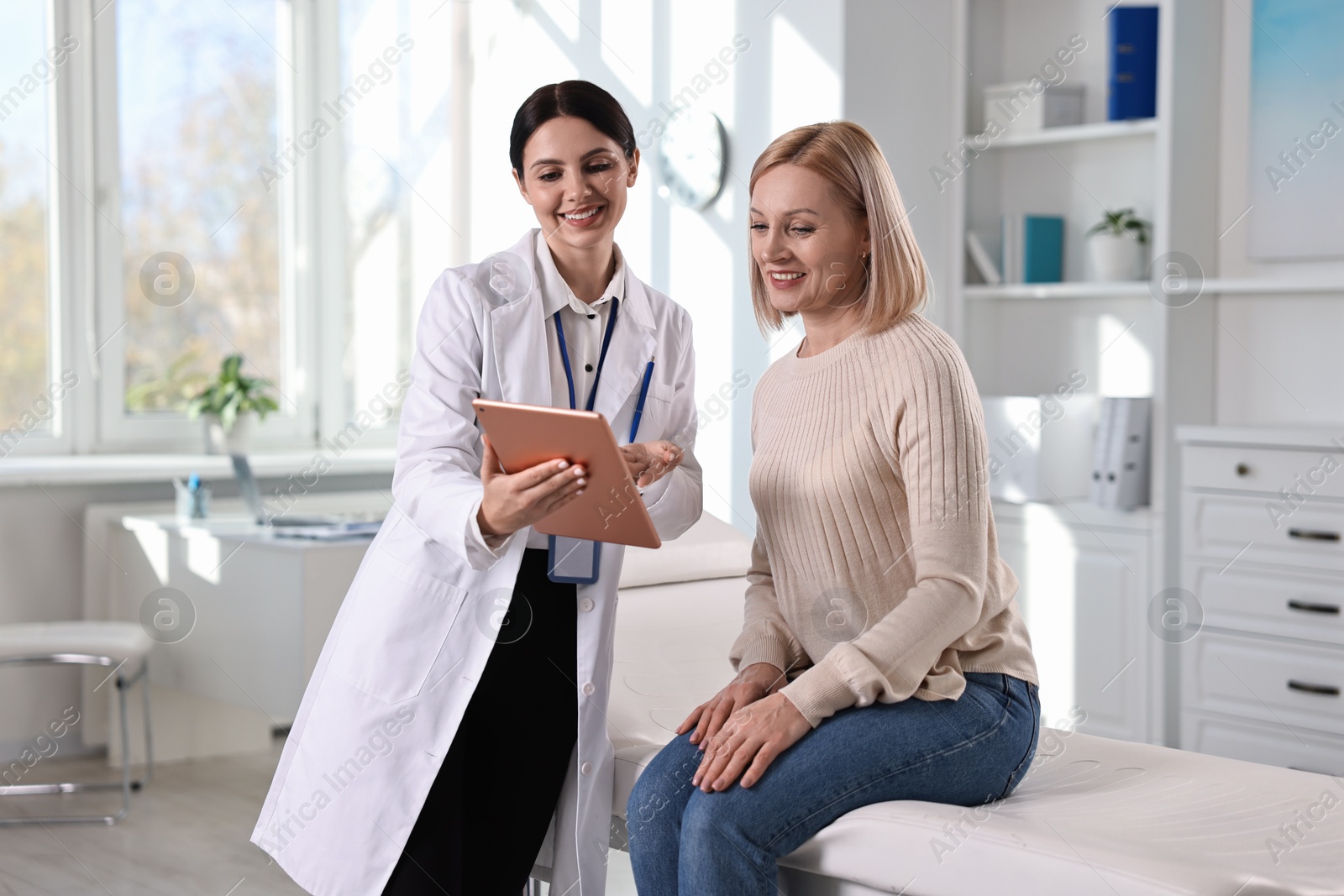 Photo of Doctor with tablet consulting woman in clinic