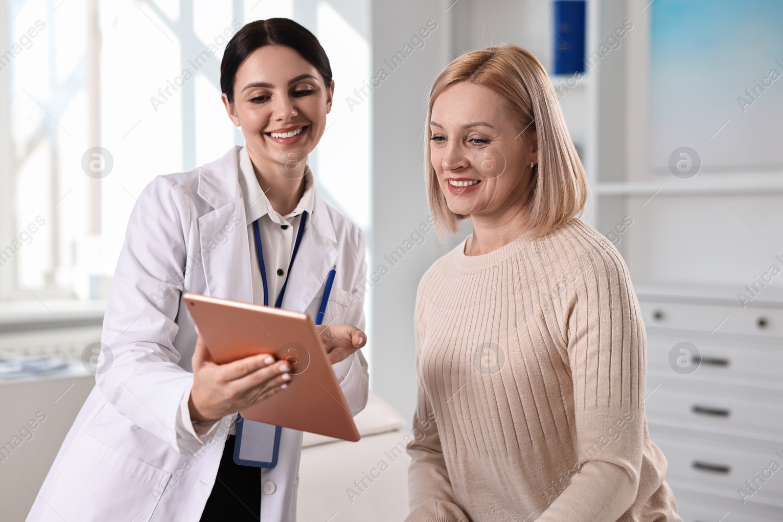 Photo of Doctor with tablet consulting woman in clinic