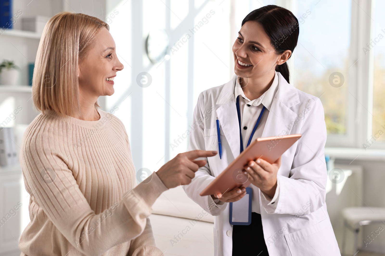 Photo of Doctor with tablet consulting woman in clinic