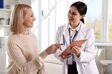 Photo of Doctor with tablet consulting woman in clinic