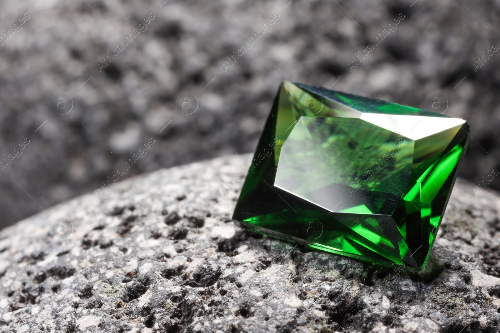 Photo of Beautiful shiny green gemstone on stone, closeup. Space for text