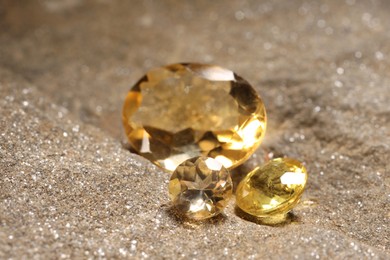 Photo of Beautiful shiny gemstones on sand, closeup view