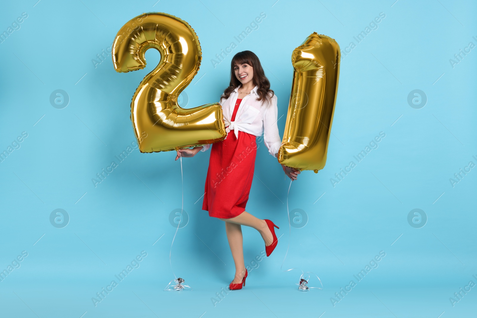 Photo of Coming of age party - 21st birthday. Young woman holding number shaped balloons on light blue background