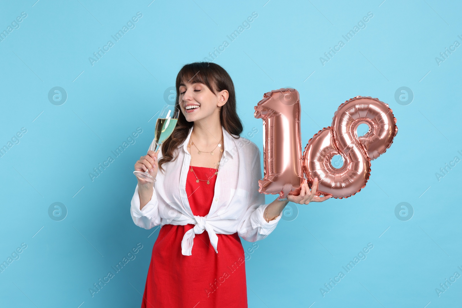 Photo of Coming of age party - 18th birthday. Young woman with glass of wine holding number shaped balloons on light blue background