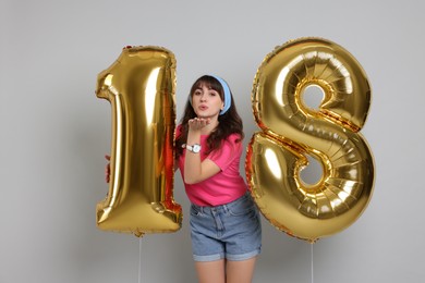 Photo of Coming of age party - 18th birthday. Young woman holding number shaped balloons on light grey background