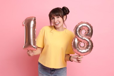 Photo of Coming of age party - 18th birthday. Young woman holding number shaped balloons on pink background