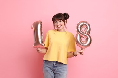 Coming of age party - 18th birthday. Young woman holding number shaped balloons on pink background