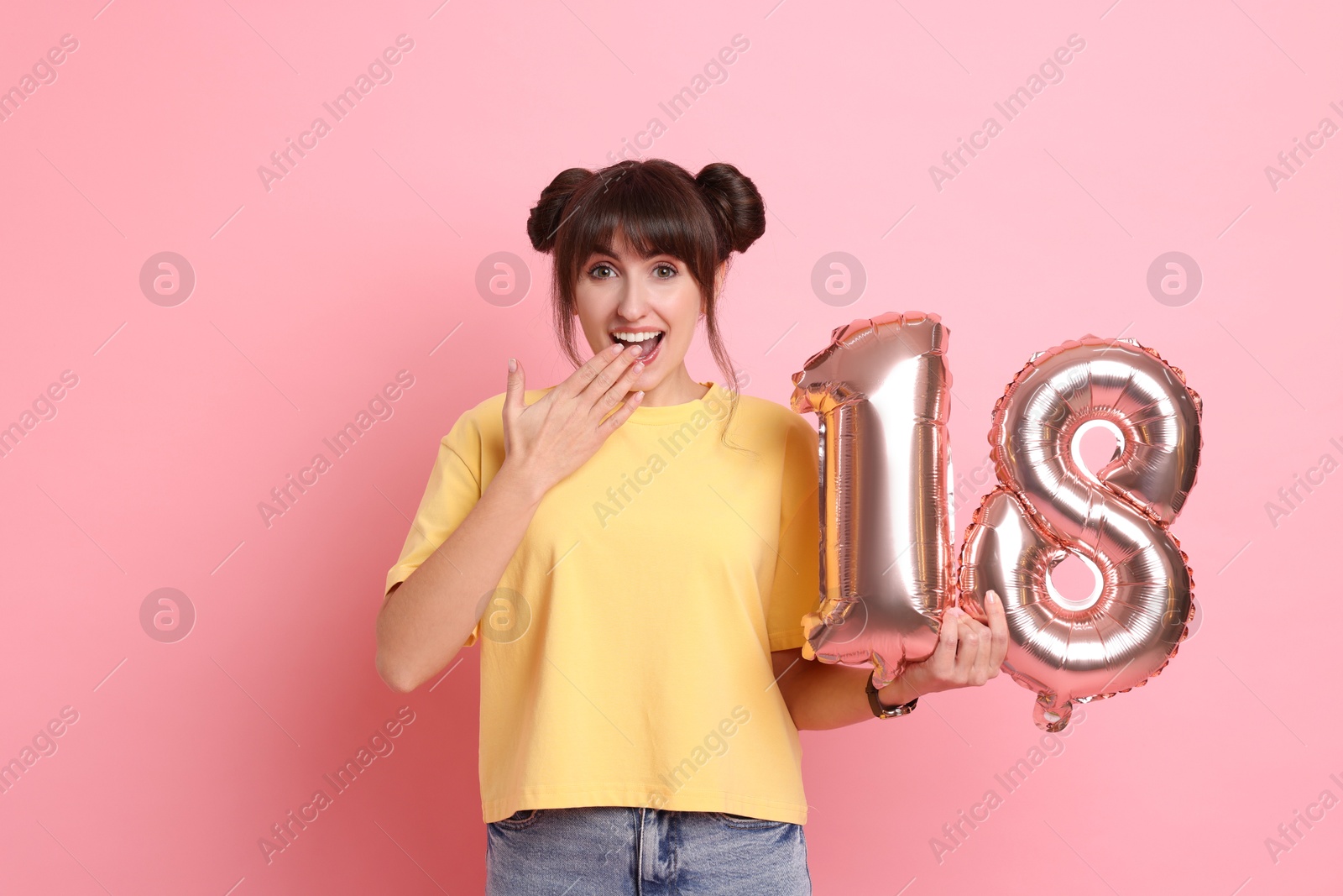 Photo of Coming of age party - 18th birthday. Young woman holding number shaped balloons on pink background