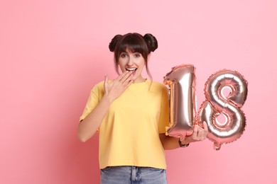 Coming of age party - 18th birthday. Young woman holding number shaped balloons on pink background