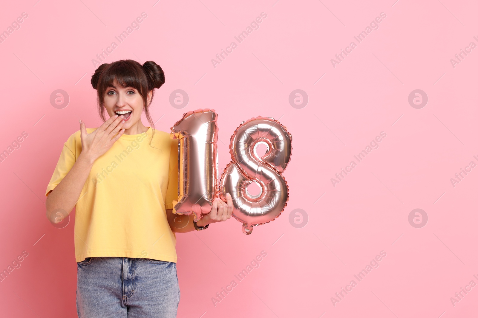 Photo of Coming of age party - 18th birthday. Young woman holding number shaped balloons on pink background, space for text