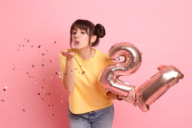 Photo of Coming of age party - 21st birthday. Young woman holding number shaped balloons on pink background with confetti