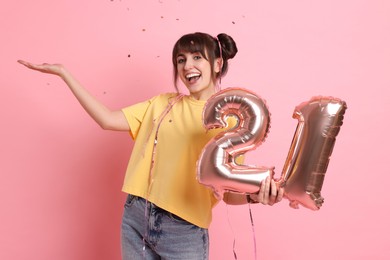 Photo of Coming of age party - 21st birthday. Young woman holding number shaped balloons on pink background with confetti