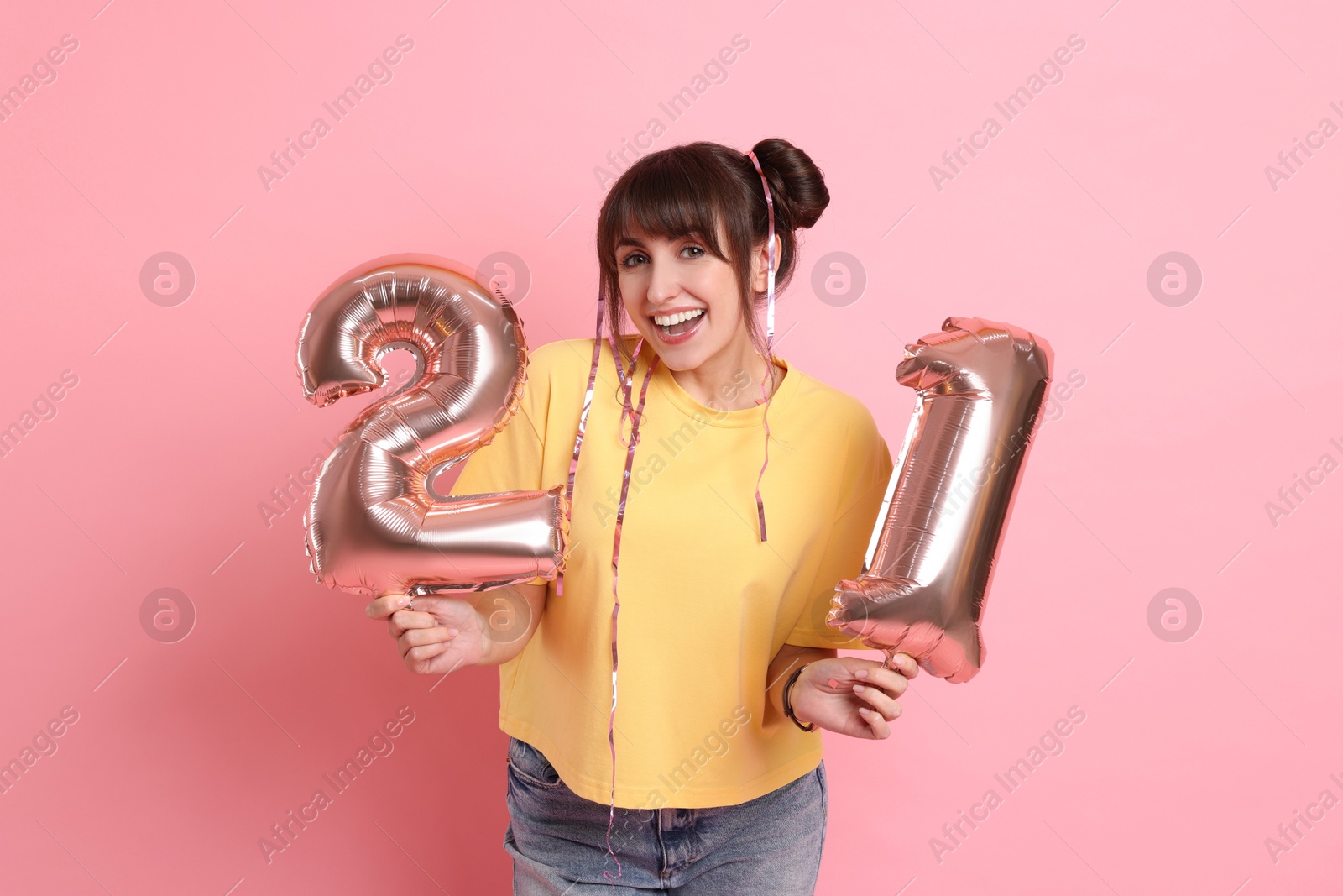 Photo of Coming of age party - 21st birthday. Young woman holding number shaped balloons on pink background