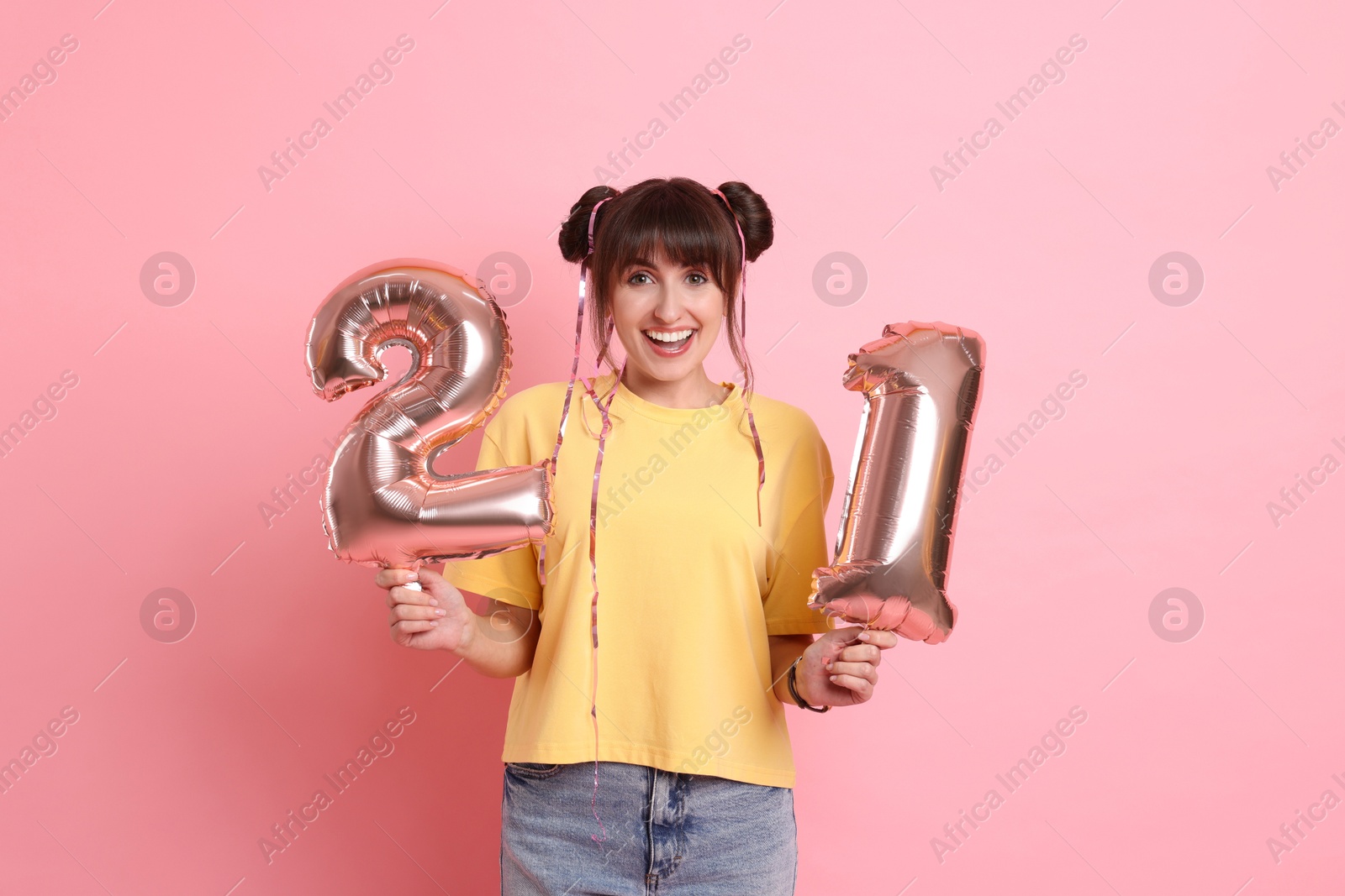 Photo of Coming of age party - 21st birthday. Young woman holding number shaped balloons on pink background