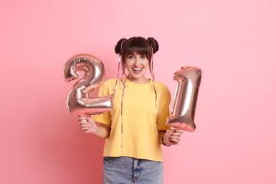 Photo of Coming of age party - 21st birthday. Young woman holding number shaped balloons on pink background