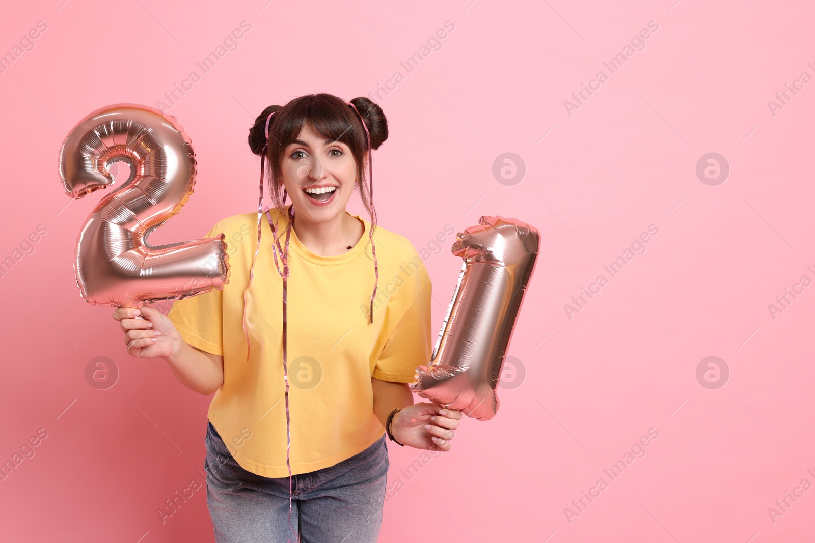 Photo of Coming of age party - 21st birthday. Young woman holding number shaped balloons on pink background, space for text