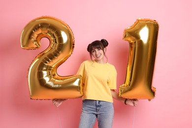 Coming of age party - 21st birthday. Young woman holding number shaped balloons on pink background