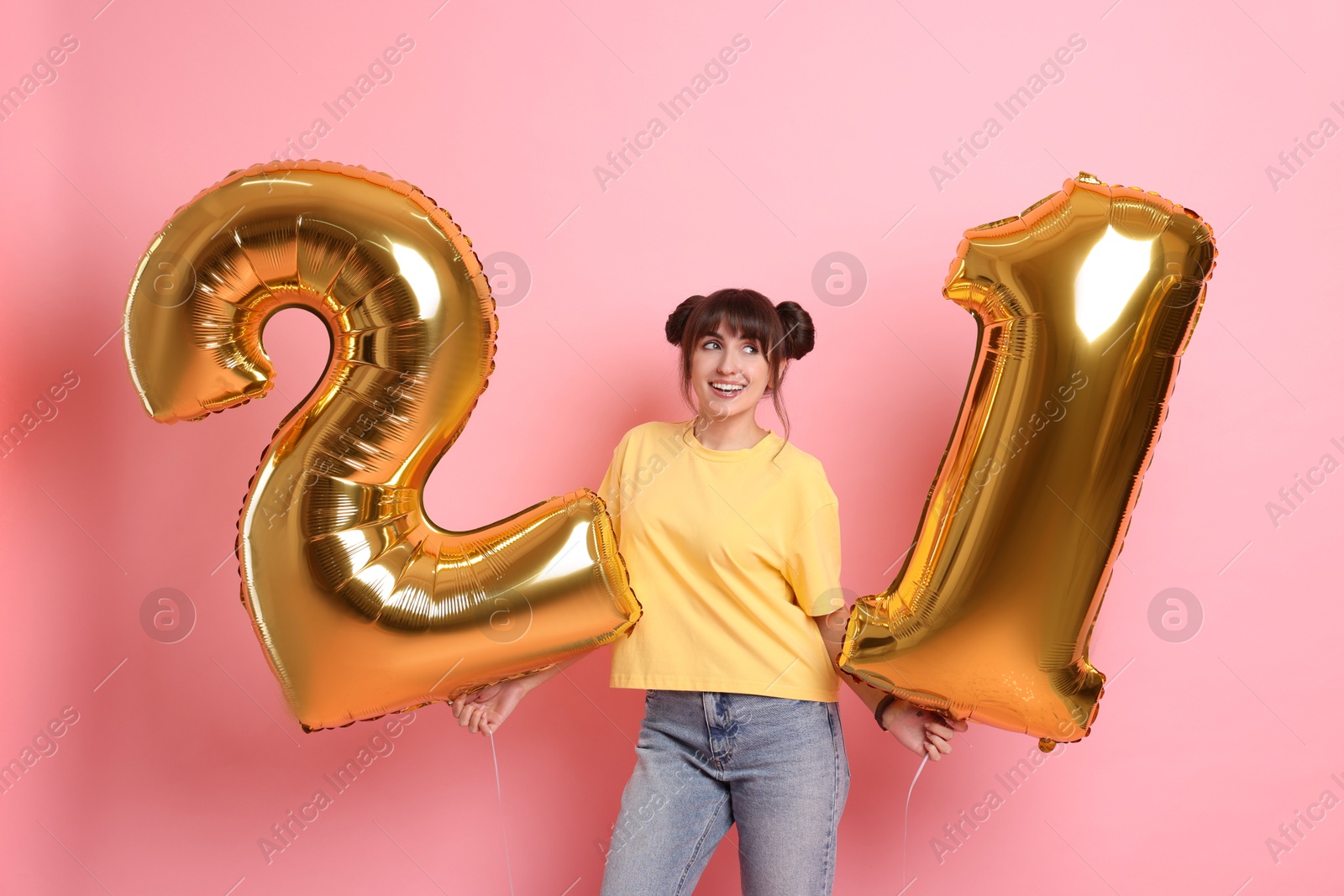 Photo of Coming of age party - 21st birthday. Young woman holding number shaped balloons on pink background