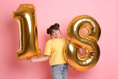 Photo of Coming of age party - 18th birthday. Young woman holding number shaped balloons on pink background