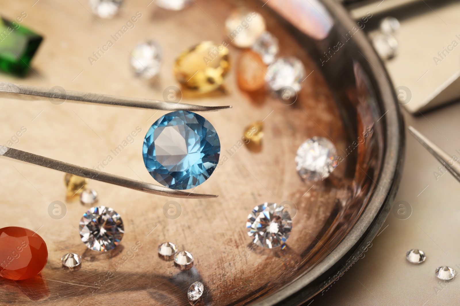 Photo of Tweezers with beautiful gemstones on light table, selective focus