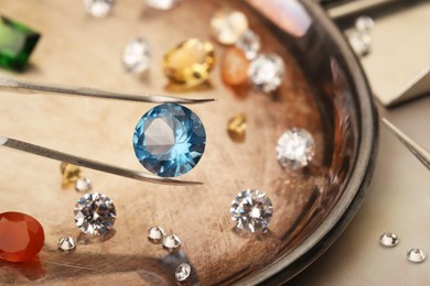 Photo of Tweezers with beautiful gemstones on light table, selective focus