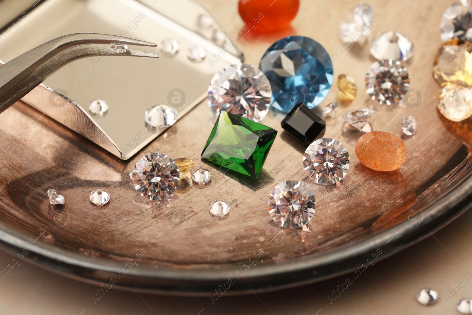 Photo of Tray with beautiful gemstones and tweezers on light table, closeup