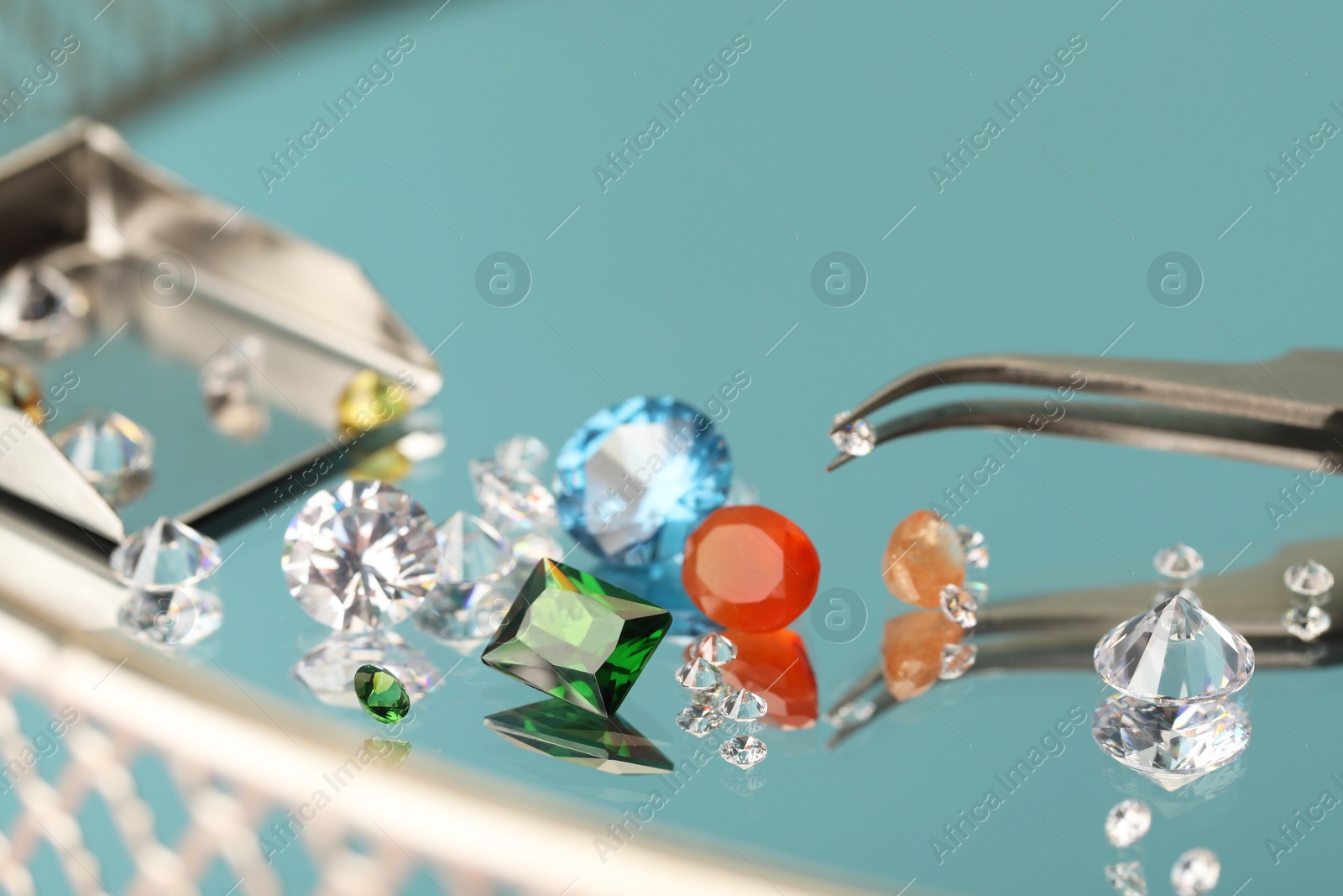 Photo of Beautiful colorful gemstones and tweezers on mirror surface, closeup