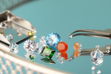 Photo of Beautiful colorful gemstones and tweezers on mirror surface, closeup