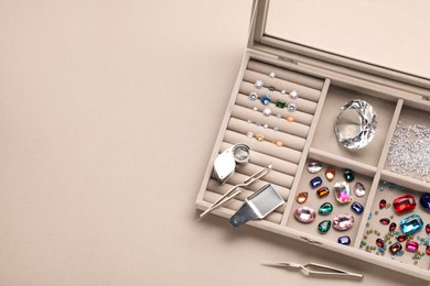 Box with beautiful gemstones and jeweler's tools on light background, top view. Space for text