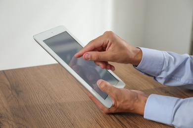 Photo of Businessman using tablet at wooden table, closeup. Modern technology