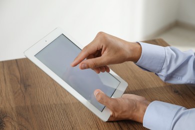 Photo of Businessman using tablet at wooden table, closeup. Modern technology