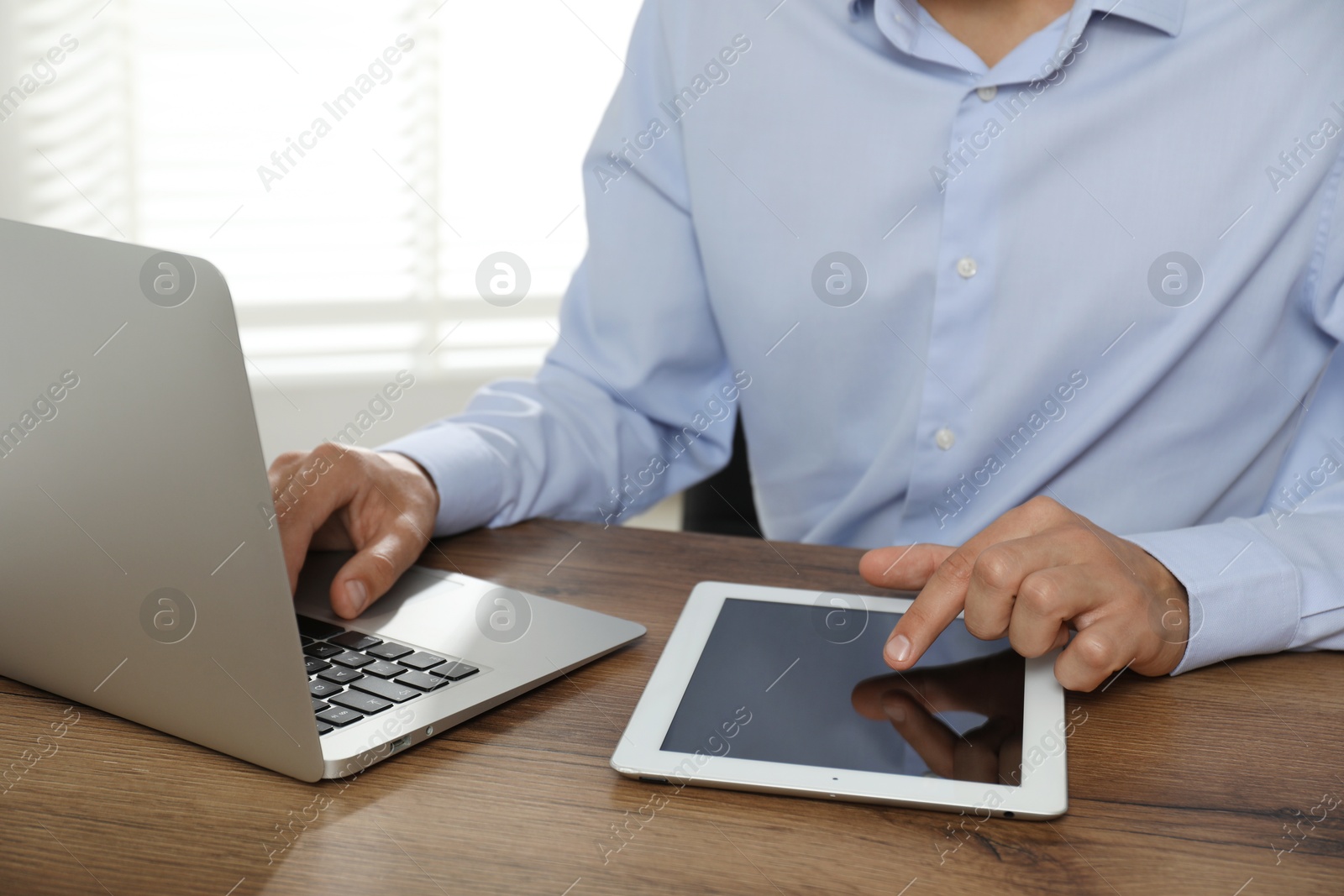 Photo of Businessman using laptop and tablet at wooden table, closeup. Modern technology