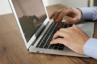 Photo of Businessman using laptop at wooden table, closeup. Modern technology