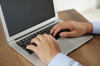 Photo of Businessman using laptop at wooden table, closeup. Modern technology