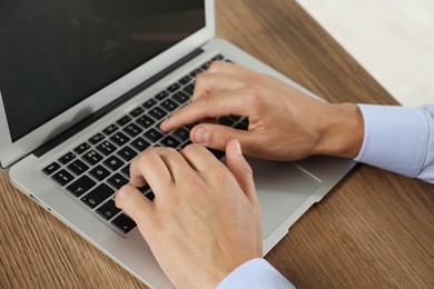 Photo of Businessman using laptop at wooden table, closeup. Modern technology