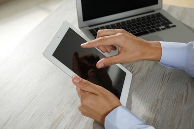 Photo of Businessman with tablet and laptop at wooden table, closeup. Modern technology