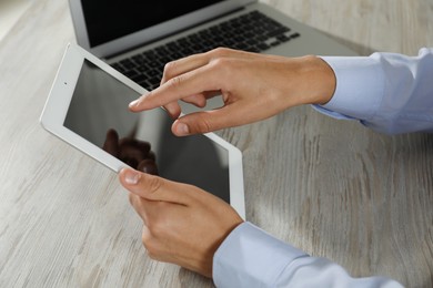 Photo of Businessman with tablet and laptop at wooden table, closeup. Modern technology