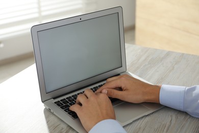 Photo of Businessman using laptop at wooden table, closeup. Modern technology