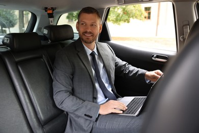 Smiling man with laptop in modern car