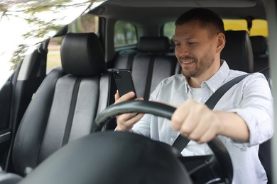 Photo of Man using smartphone while driving modern car, view through windshield